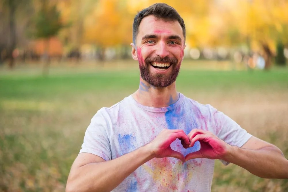 Hombre feliz y untado de pintura hace señal de corazón con sus manos