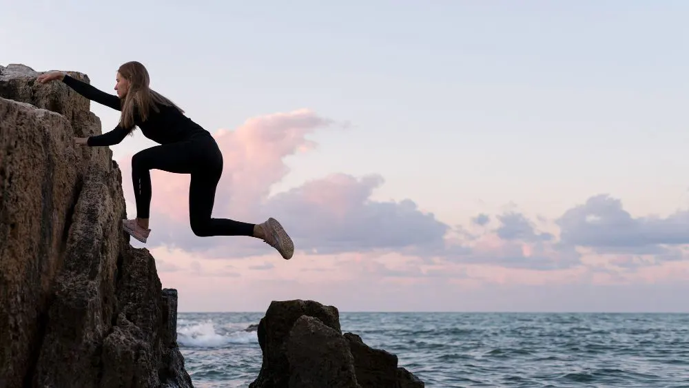 Mujer escalando rocas en el mar